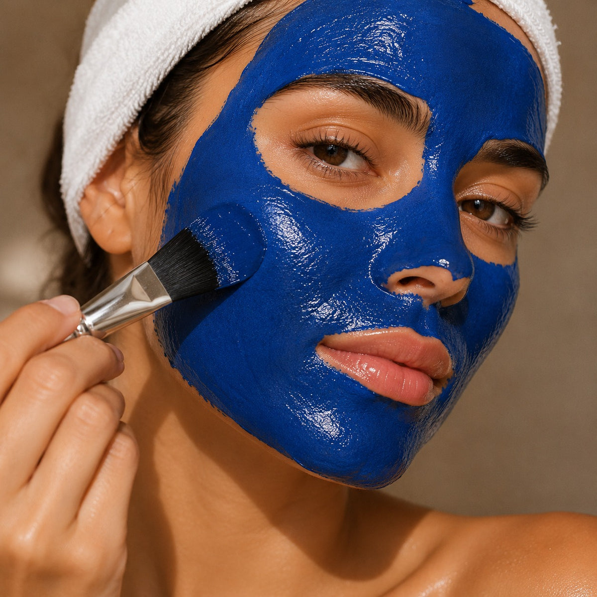 Woman applying blue facial mask to her face with a brush.