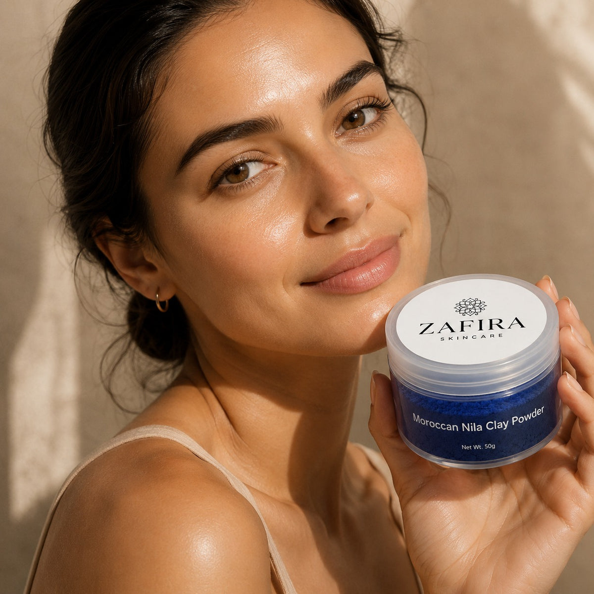 Woman holding a jar of Zafira Skincare Moroccan Nila Clay Powder against a neutral background